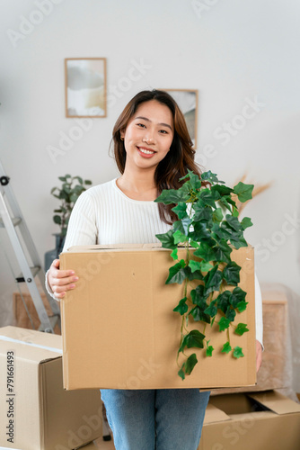 Woman smiling and holding a moving box with a plant photo