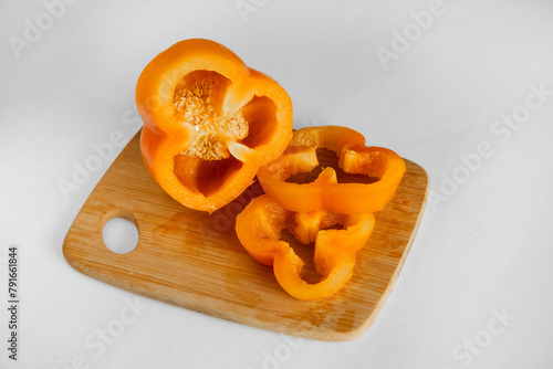 Slices of juicy sweet orange pepper on wooden board on white background