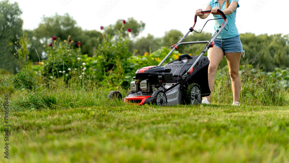 girl with a lawn mower mows the lawn in front of the house girl with a lawn mower mows the lawn in front of the house