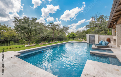 A large, simple pool in the backyard of an upperclass home with a concrete patio and trees and a blue sk
