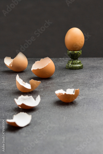 Brown egg on egg stand. Eggshells on table