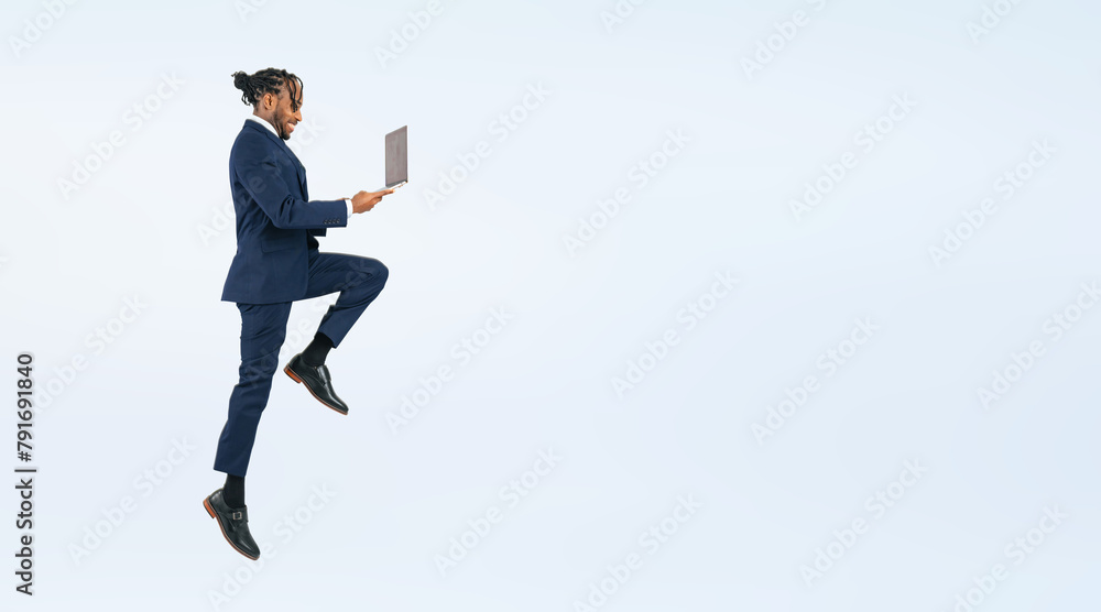 Full body photo of a black male businessperson jumping while looking at a laptop. (We also sell PNGs that are cropped and have transparent background. Please search for 