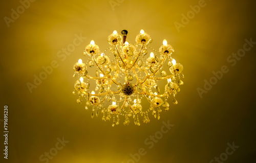 Close-up of classic crystal lamp hanging in the house, hotel or restaurant. Crystal lamp with gold, yellow colored light. Luxury light lamp with dark brown background. 