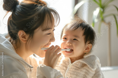 Asian mother brushing teeth baby toddler. Cosy bathroom with natural light, mom and child happy and playful atmosphere. Hygiene for children, childcare. Daily routine