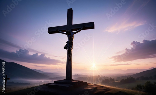 a cross with a statue of jesus on a hill with sunlight in the far back