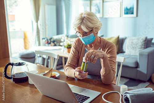 Senior woman with face mask using laptop and feeling unwell at home photo