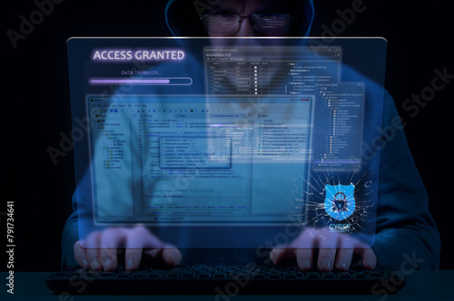 Man in hood on dark background uses keyboard and virtual screen to break cybersecurity system