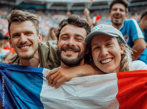  amigos franceses sosteniendo una bandera de España animando a su equipo, contentos sonriendo a cámara, con fondo de estadio olimpico deportivo con multitud de gente photo
