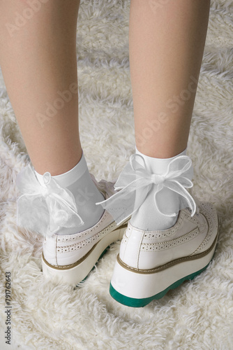 Close-up of a woman's legs wearing white socks with bows and sneakers. The girl is standing on a fur carpet. Nylon socks on the feet of a beautiful woman. Back view. 