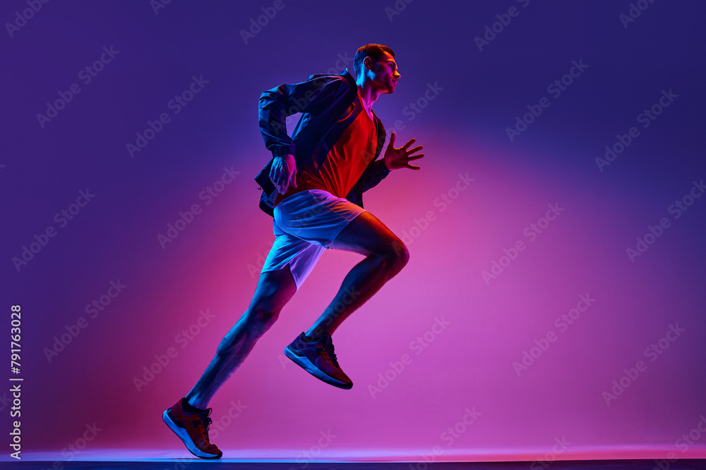 Active young man, athlete in sportswear in motion training, running on gradient pink purple background in neon light. Concept of active and healthy lifestyle, sport, hobby, motivation, endurance