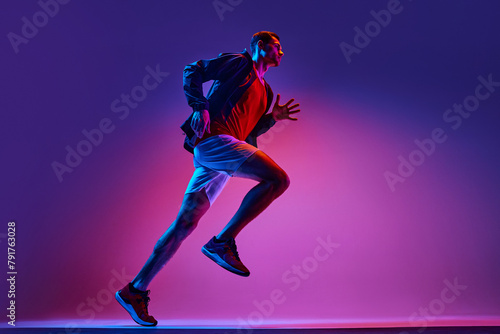 Active young man, athlete in sportswear in motion training, running on gradient pink purple background in neon light. Concept of active and healthy lifestyle, sport, hobby, motivation, endurance