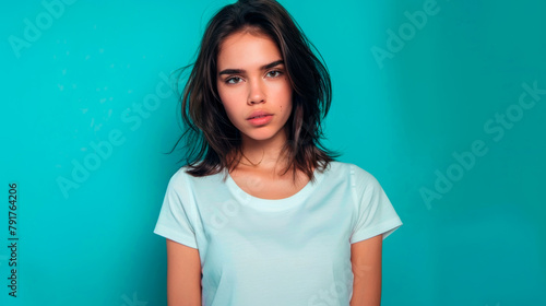 Portrait of an attractive young sad and unhappy brunette woman on a blue background with a copy space. A sweet, upset and offended girl in a simple white T-shirt. photo