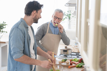 Happy young son helping his old elderly senior father in the kitchen to cook prepare meal, dinner, lunch for family. Happy father`s day! I love you, dad! Men cooking together