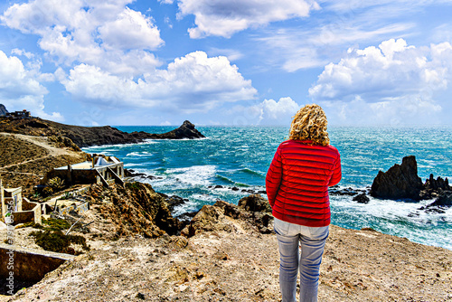 Blonde woman with curly hair looking at the horizon at the Las Sirenas reef in Cabo de Gata-Níjar, Almería, Spain