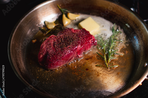 Canvas Print Steak being seared on pan on the stove with herbs and butter