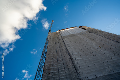 Renovation of a high-rise building. a tower crane. the building is covered with fabric during renovation.