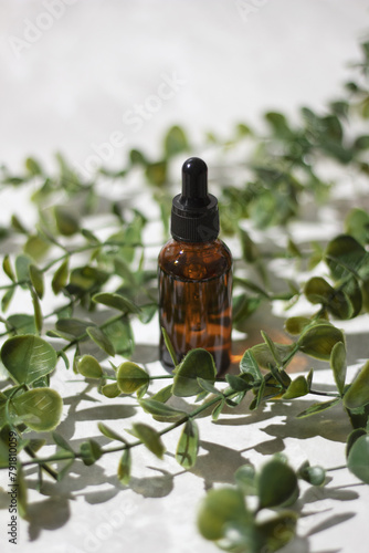 Mock up glass dropper bottle on a white podium on a white gray background with hard shadows, with leaves and stones. Cosmetic pipette on a white background.