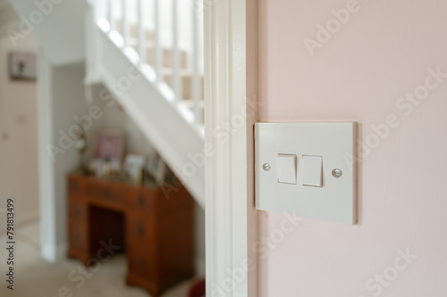Shallow focus of a two-way light switch seen looking out from the ground floor kitchen in a hallway. A staircase can be seen.
