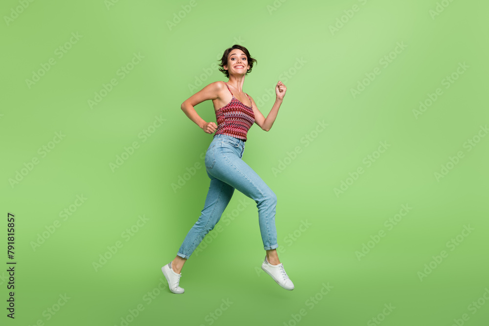 Full length photo of good mood cheerful girl wear stylish clothes running jogging going empty space isolated on green color background
