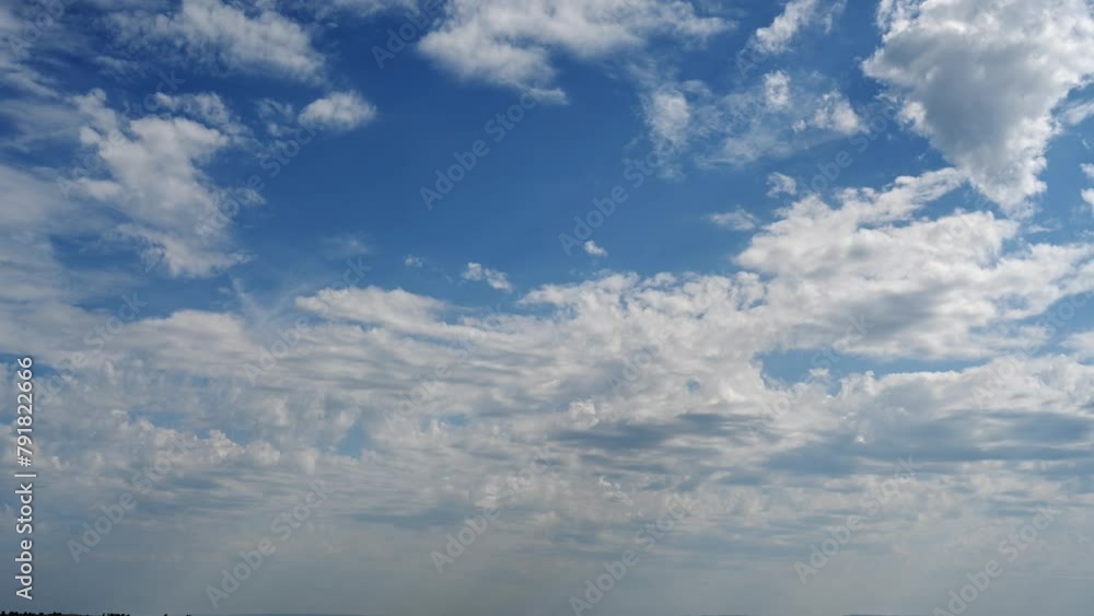 Time lapse framed just above the horizon showing a bright blue sky full of moving white summer clouds.
Time lapse framed just above the horizon showing a bright blue sky full of moving white summer clouds.