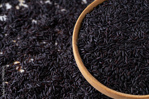 Organic raw black rice are scattered in a wooden bowl close up.