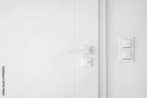 Light switches on white wall near closed room door with mechanical handle © brizmaker
