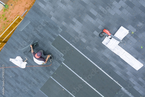 Professional roofing contractor uses an air nail gun to install new asphalt bitumen shingles on roof house