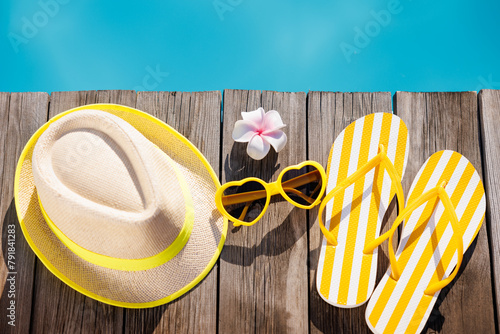 Beach hat, flip-flops and sunglasses on wooden planks near swimming pool