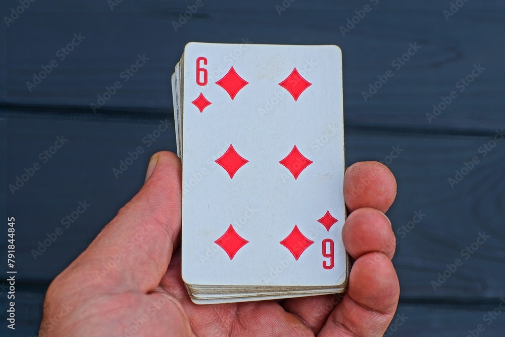 one playing paper red card diamond six in the player's hand on the background of a black table during the game