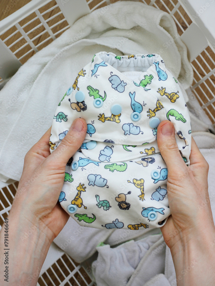 Female hands holding a cloth diaper inside a laundry basket full of