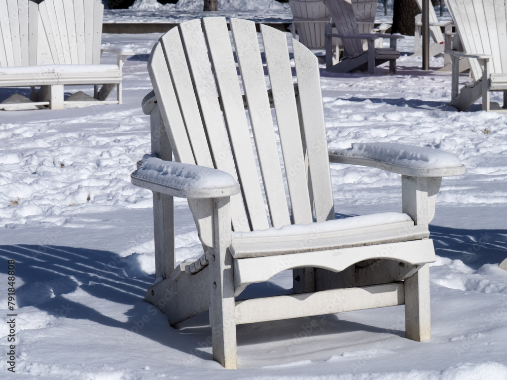 Fototapeta premium A white Adirondak chairs at a waterfront park covered in snow in winter