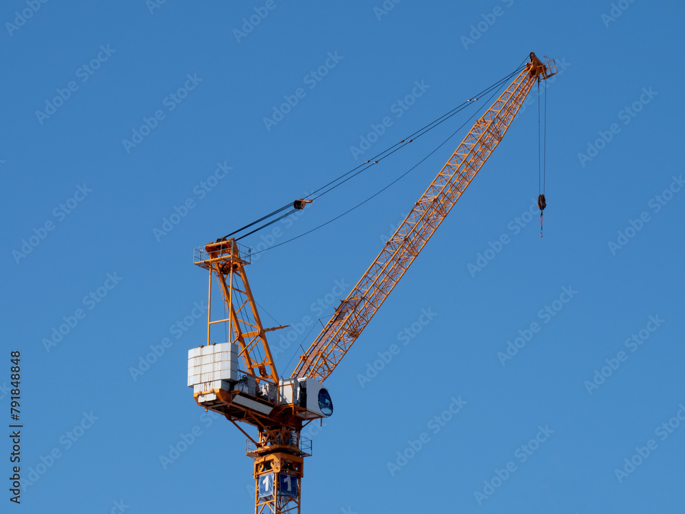 a yellow construction crane at a high rise construction site on a clear blue sky