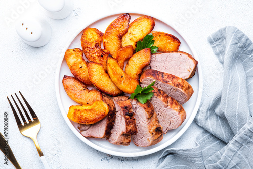 Baked pork tenderloin with caramelized apples on plate, white table background, top view