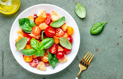 Simple summer salad with with stale bread, cherry tomatoes, olive oil, sea salt and green basil, stone table background, top view