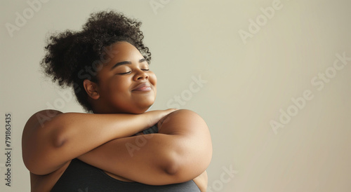 A portrait of a young individual with a serene expression, wrapped in a self-hug, suggesting inner peace and confidence on a gentle gray backdrop.