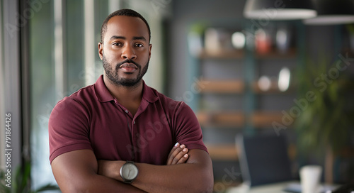 A young man stands assuredly in a bustling office setting, his arms crossed in a stance of readiness and confidence. photo