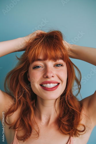 A spirited redhead with a bright smile and a carefree pose against a soothing pastel blue background  exuding vivacity and charm.