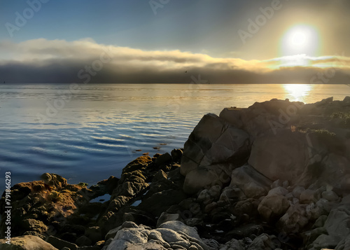 Sun rising above a fog bank and rocky beach at Monterey Bay in California © Chad