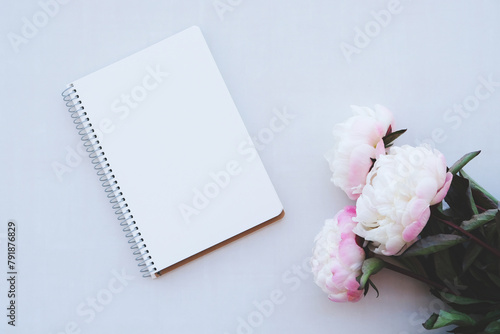 Mockup of open notebook with blank page and beautiful peony flowers in bloom on white background. Copy space. Flat lay, top view.