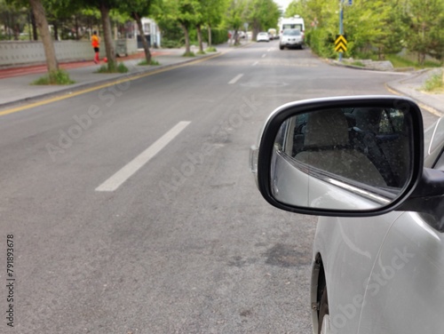 It shows a street scene seen from the perspective of a car's side mirror. The mirror reflects the interior of the car, including the side mirror, which is angled to show the road ahead. © fatih