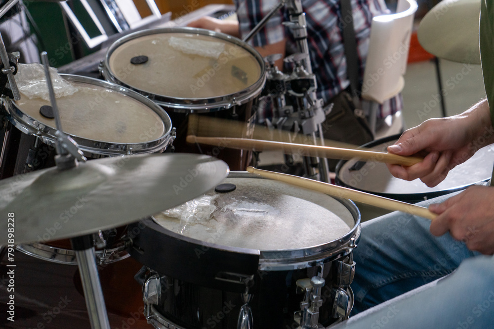 Close-up of a man's hands playing drums. His drumsticks hit with energy, showing the rhythm and motion of live performance. Cymbals and drumheads are slightly blurred, indicating movement. Close-up of a man's hands playing drums. His drumsticks hit with energy, showing the rhythm and motion of live performance. Cymbals and drumheads are slightly blurred, indicating movement.