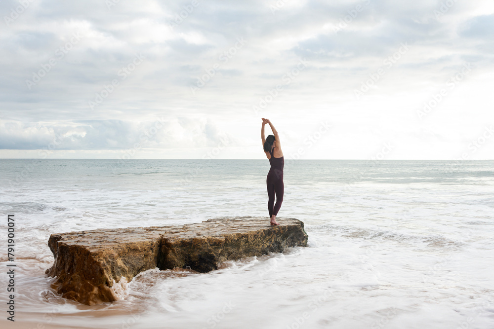 woman free swimmer doing stretching exercise on a rock before entering the sea.