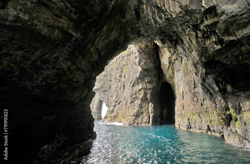 Rocks and caves of the coast near the famous spireTrøllkonufingur towering rock formation on Vágar Island