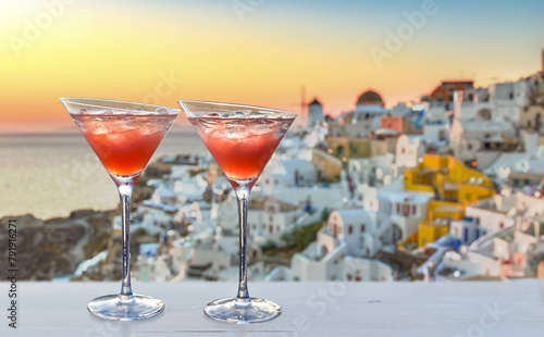 two red cocktails with ice cubes, blurred lights of the greek island Santorini in the background