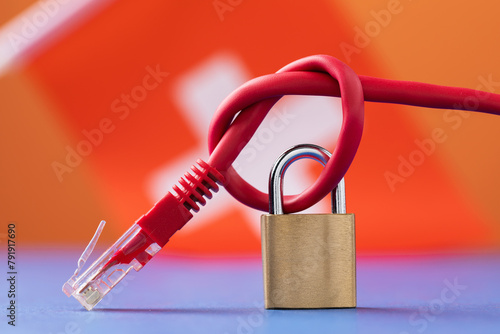 A closed lock on a tied network wire into a knot against the background of the Swiss flag, the concept of security of Internet technologies in the country
