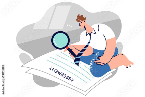 Man lawyer reads large agreement and uses magnifying glass to scrutinize business documents