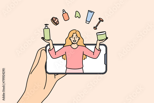Woman beauty blogger juggles with cosmetics, looking out from mobile phone screen, giving tips on applying makeup. Girl beauty blogger tells lifehacks for facial skin care or getting rid of wrinkles