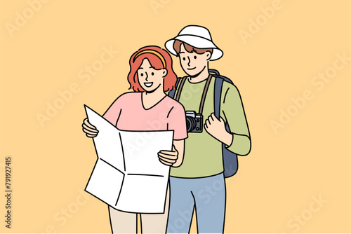 Couple of tourists study map, choosing route for hike in mountains with wildlife or walk along city streets. Tourists with photo camera use paper map for navigation and orientation on terrain.