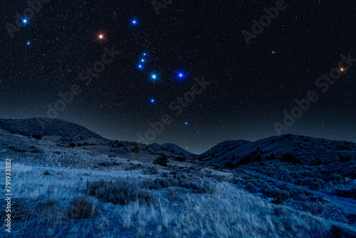 Starry nightscape with the Orion constellation glowing over a mountainside © Boyce