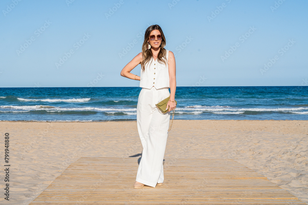 Elegant woman with sunglasses and white dress posing on the beach on a sunny day Elegant woman with sunglasses and white dress posing on the beach on a sunny day